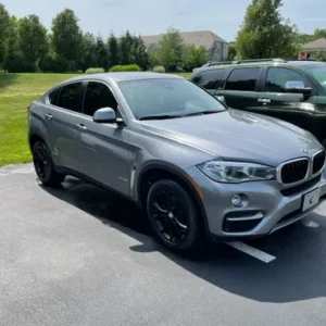 A sleek silver sports utility vehicle, freshly enhanced with auto detailing, parked outdoors on a sunny day with a clear sky and residential backdrop.
