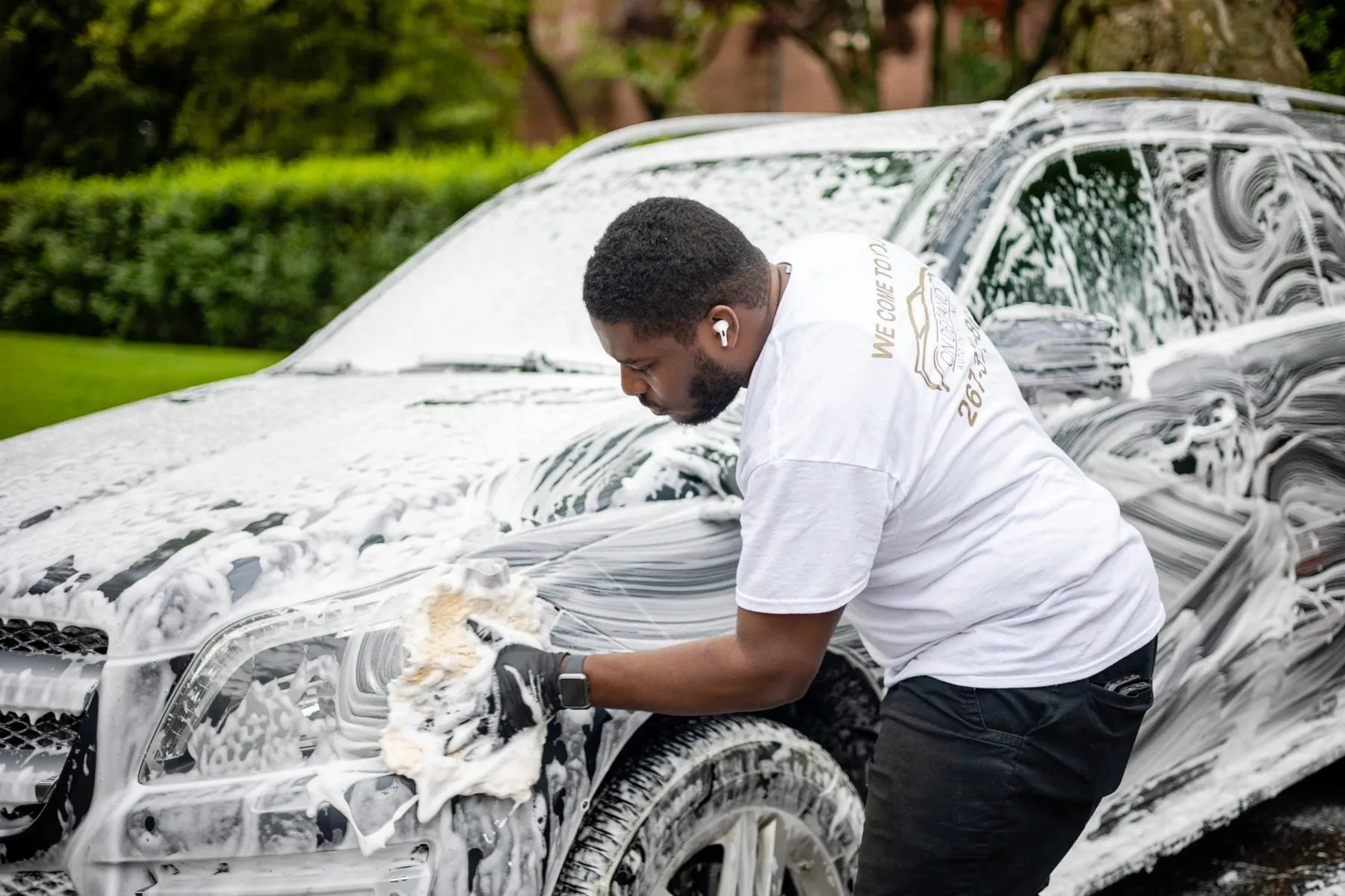 a man in white shirt washing a car with foam
