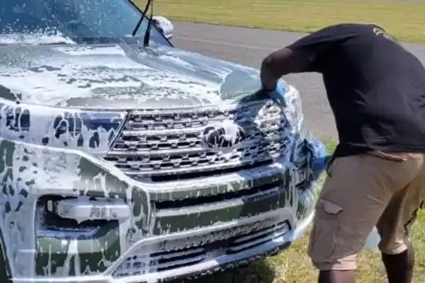 Man performing auto detailing on a sud-covered car on a sunny day.